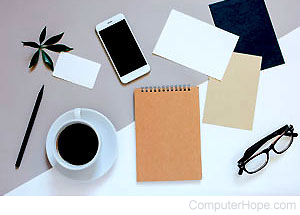Smartphone, tablet, notebook, and coffee cup on a table, representing a workspace.